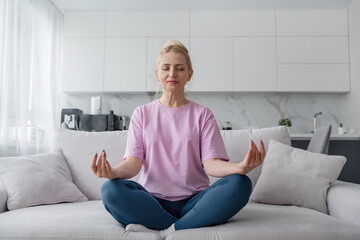 Fototapeta premium Elderly lady does yoga on the sofa in modern living room, enhancing mental and physical wellbeing