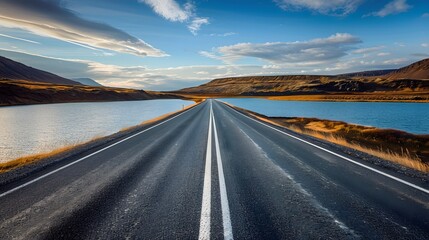 Naklejka premium Diminishing perspective of asphalt empty roadway with road markings passing through scenic lake against sky in iceland. 