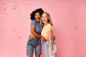 Two attractive young women in cozy attire standing next to each other against a vibrant pink...