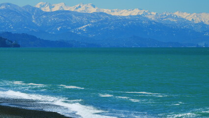 Snow-Capped Mountain Peaks And Sea. Snow-Capped Mountain Range Against Blue Sky. Still.