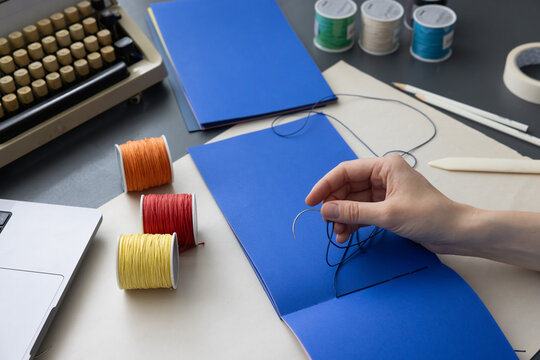 High-quality image of a person binding a book using traditional coptic stitch technique. DIY bookbinding, handcrafting, artisan book, handmade, coptic stitch, binding tools, creative, detailed process