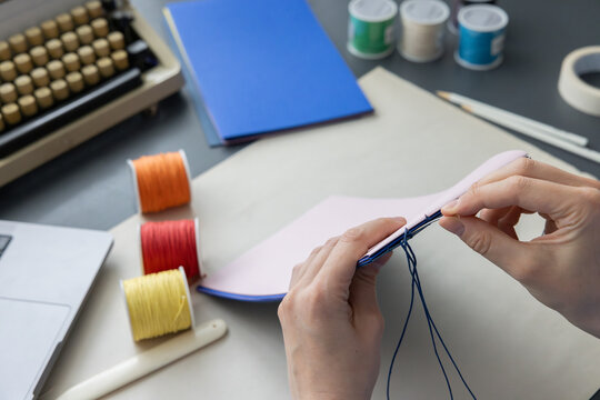 High-quality image of a person binding a book using traditional coptic stitch technique. DIY bookbinding, handcrafting, artisan book, handmade, coptic stitch, binding tools, creative, detailed process