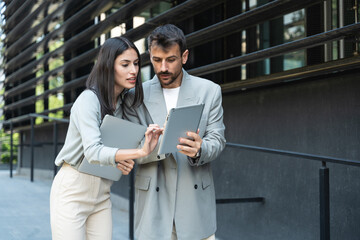 Business man and woman out of office building with laptop and digital tablet. Technology used in modern business life. Sustainable energy experts developers and design professionals working together.