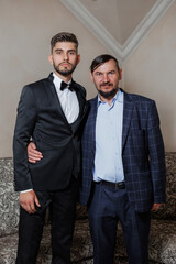 Two men in suits are posing for a picture. One of them is wearing a tie. The man on the left is wearing a black suit and the man on the right is wearing a blue suit