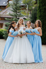 A bride and her bridesmaids are posing for a picture in front of a building. The bride is wearing a white dress and a blue veil