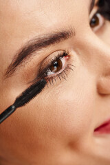 Close-up portrait of an attractive woman applying makeup with a mascara near her eye.