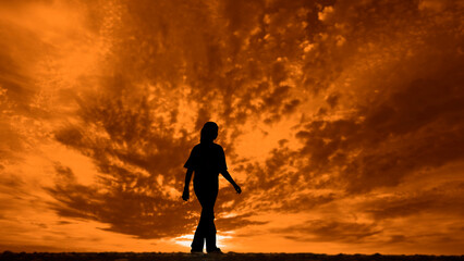 black silhouette of one girl walking dramatic orange yellow sunset or sunrise with clouds background,  golden dark cloudy sky at sunset. nature backdrop. alone female woman walk along horizon line