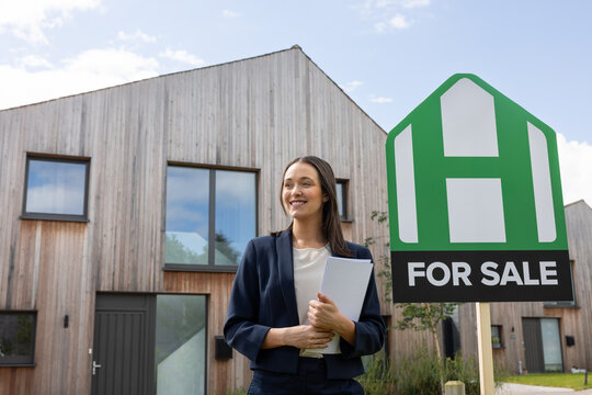 Real estate agent standing on a street with a house for sale