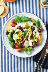 Mediterranean salad with mozzarella, olives, basil and grilled vegetables on a blue striped linen tablecloth