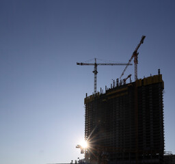 construction in sun rays of sunset. tower cranes silhouettes over amazing blue sunset sky. sunrays...