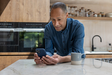 Happy mature african american man using a smartphone in his kitchen