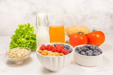 Healthy breakfeast concept. Oatmeal cereal porridge with fresh berries and nuts in white bowl, vegetable and juice. Dietary. Top view on white marble stone table. 