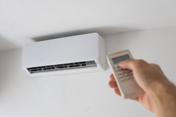 Close-up of a man's hand holding the remote control from the air conditioner that hangs on a white wall in the apartment. High quality photo