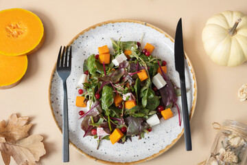 Plate with salad with greens, pumpkin and soft cheese on beige background top view