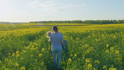 Happy Caucasian Farmer Family Funny A Mother Holds Son In Her Arms Little Boy. A Mother Walks With Her Son In Her Arms Through A Rapeseed Field.