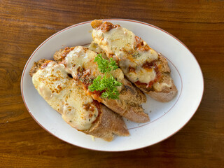 Cheesse mozzarella bruschetta with minced meat and Italian pepper and herbs, served on a white plate, on top of wooden table.