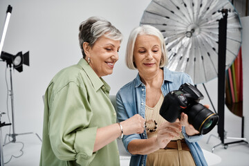 Two women, a photographer and her model, review photos in a studio setting.