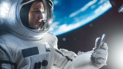 Man in a Space Suit Casually Talking on a Phone in Outer Space While Servicing A Satellite. Astronaut Chatting with Mission Control Crew, Family or Work Colleagues on a Video Call on a Smartphone