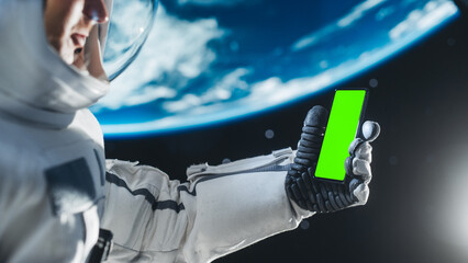 Young Astronaut Floating in Space in Zero Gravity. Spaceman Using Mobile Phobe With Green Screen Chromakey On Display. Professional Engineer Using Smartphone in Open Space Outside Orbiting Spacecraft. © Gorodenkoff