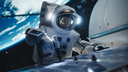 Portrait of a Handsome Young Astronaut Investigating a Solar Panel on a Satellite in Outer Space. Trained Professional in a Space Suit Performing Extravehicular Activity Outside the Spacecraft