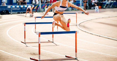 Naklejka premium female runner running 400 meters hurdles race in summer athletics championships