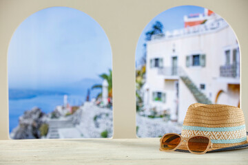 Obraz premium Towels and straw summer hat on wooden table top with copy space for products. Arched windows and blurred buildings of summer resort background.
