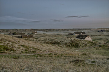 thatched houses scattered in the dunes when the fog settles in the evening