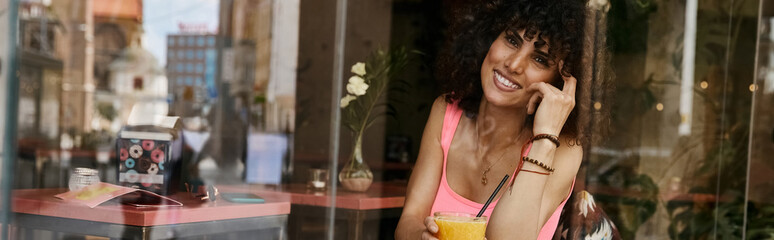 A smiling woman enjoys a beverage at a cafe in Europe.
