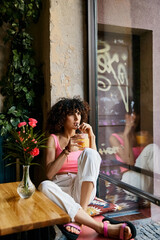 A woman in stylish attire enjoys a drink while sitting by a window in a European cafe.