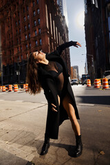 A woman in a long black coat dances in the streets of New York City.