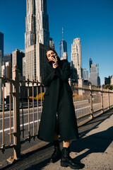 Woman in black coat dances on NYC street amid skyscrapers.