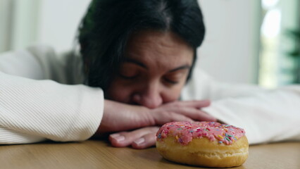 A woman lying on a table, thoughtfully gazing at a colorful sprinkled donut, highlighting the theme of delayed gratification and temptation, with a contemplative and reflective expression