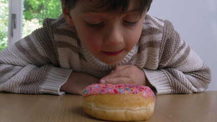 A young boy leaning over a table, licking a colorful sprinkled donut, blending the themes of playful indulgence and temptation with a curious and eager expression