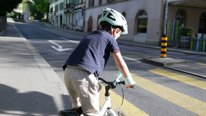 Boy on bicycle wearing protective helmet cycling on city street with crosswalk and vehicles, emphasizing safe cycling practices and active childhood in urban settings, perfect for health 