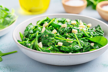 A white bowl filled with green spinach and cheese
