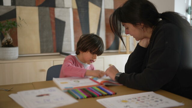 Child and parent studying together at a table, focused on a colorful workbook, highlighting the significance of educational activities and parental guidance in a home environment