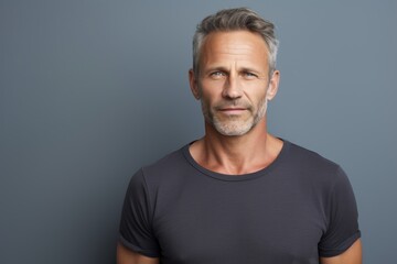 Obraz premium Portrait of a smiling man in his 50s dressed in a casual t-shirt while standing against bare monochromatic room