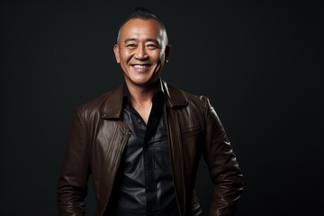 Obraz premium Portrait of a grinning asian man in his 50s sporting a stylish leather blazer while standing against bare monochromatic room
