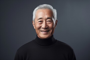 Portrait of a grinning asian man in his 70s wearing a classic turtleneck sweater while standing against bare monochromatic room