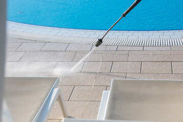 A high-pressure water jet cleaning the poolside area, enhancing the shine of the lounge chairs...