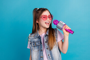 Photo portrait of charming little girl sing karaoke sunglass wear trendy jeans outfit isolated on blue color background