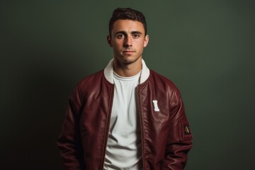 Fototapeta premium Portrait of a tender man in his 30s sporting a stylish varsity jacket in front of plain cyclorama studio wall
