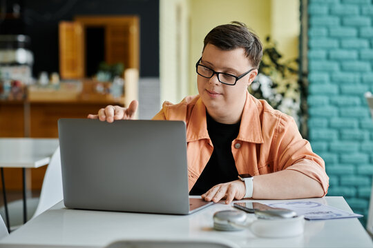 A young man with Down Syndrome is working on his laptop in a cafe, focused on his task.