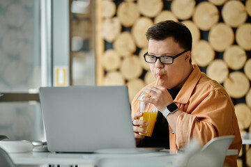 A man with Down syndrome sits in a cafe, working on his laptop while enjoying a refreshing drink.