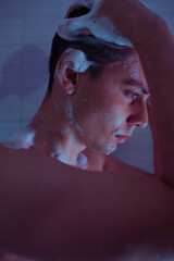 handsome young man washes himself under a cold shower in the bathroom. Drops of water flow down the...