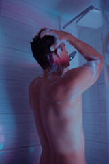 handsome young man washes himself under a cold shower in the bathroom. Drops of water flow down the...