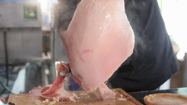 unrecognizable professional person cutting a steaming piece of galician lacon or sliced cooked ham to prepare a tapa. Traditional food from galicia. spanish food.