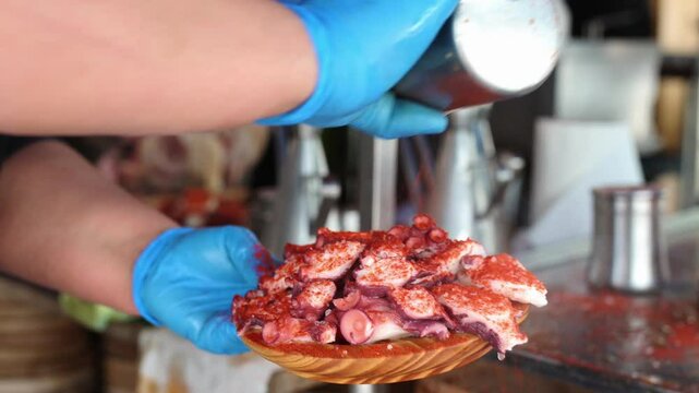 unrecognizable professional person pouring paprika and olive oil over a Galician-style octopus tapa. Traditional food from the north of Spain.
