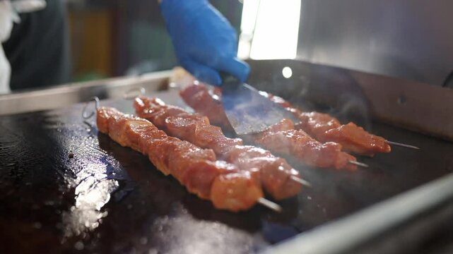 unrecognizable professional person preparing a portion of "pinchos morunos" (pork loin meat carved on a skewer) on the griddle of a restaurant. Traditional Spanish cuisine