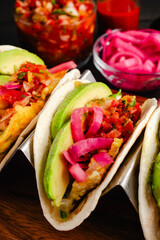 Tex-Mex Migas Breakfast Tacos in a Taco Holder Close-up: Overhead view of breakfast tacos with eggs, sliced avocado, pickled onions, and salsa